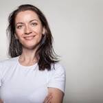 Portrait of a confident woman smiling with arms crossed, wearing a white t-shirt on a gray background.