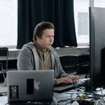 A dedicated programmer focused on coding at his workspace with dual monitors in a modern office setting.