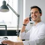 A cheerful call center agent wearing headphones works at a modern office desk.